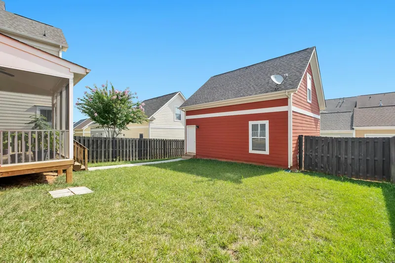 Red backyard cottage behind a house with a fenced lawn