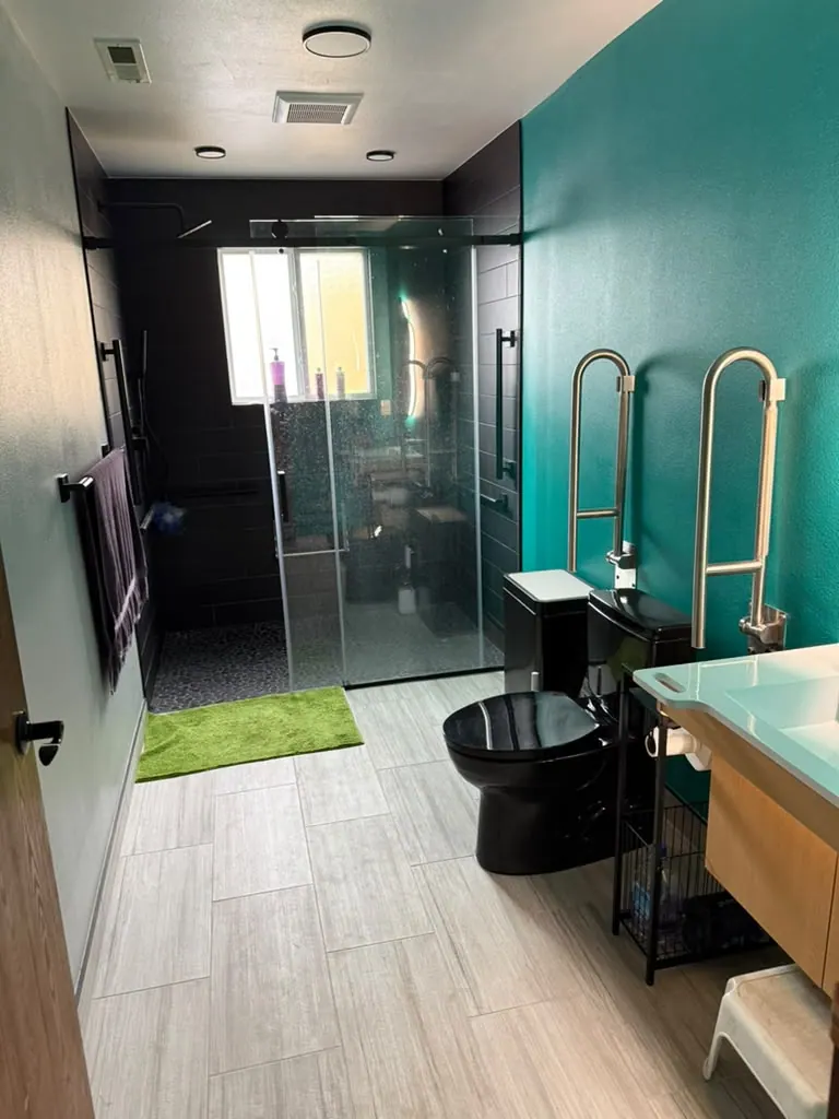 Converted full bathroom with a glass shower, a teal accent wall, a black toilet and grab bars