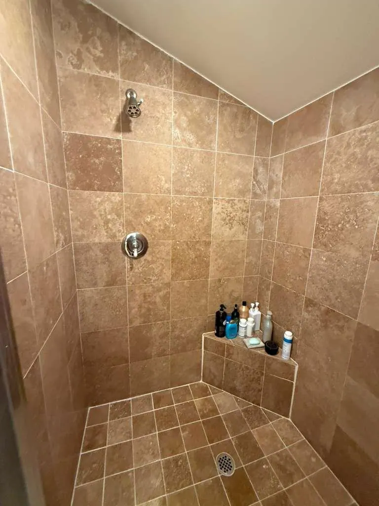 Before: The shower before the remodel, with brown square tile on the walls and floor