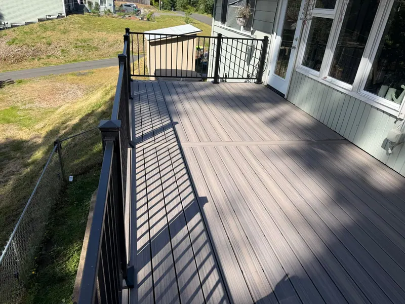 After: Long composite deck along the side of the house, with black metal railings and a border board across the decking