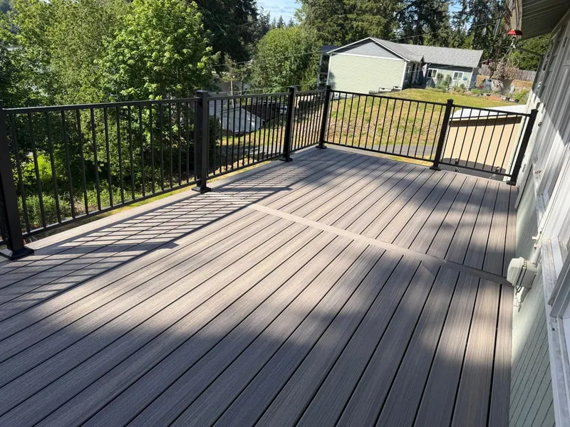 Finished composite deck with black metal railings and a border board across the decking, looking out over the yard