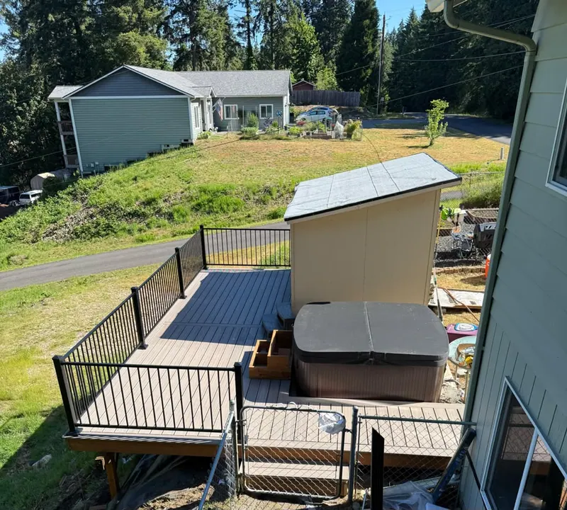 After: Raised composite deck built around a hot tub next to a shed, with black metal railings