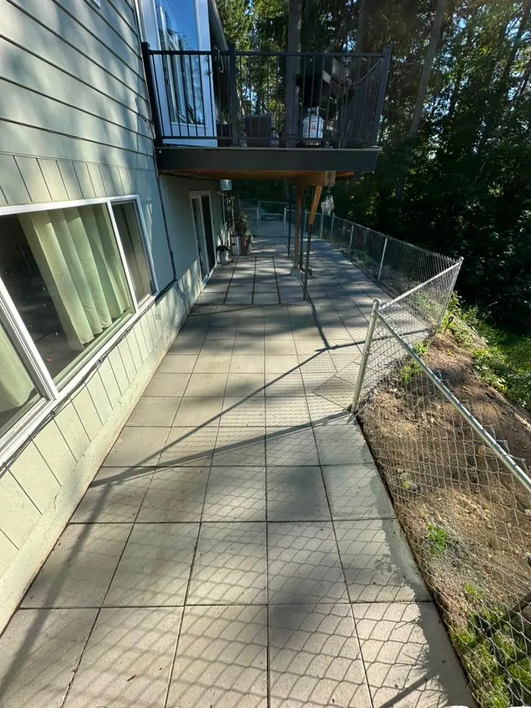 Paver walkway along the side of the house, between the wall and a chain-link fence on the slope