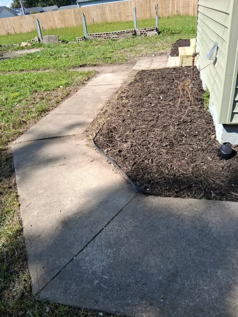 New mulched planting bed with black edging along the house, beside a concrete walkway and lawn